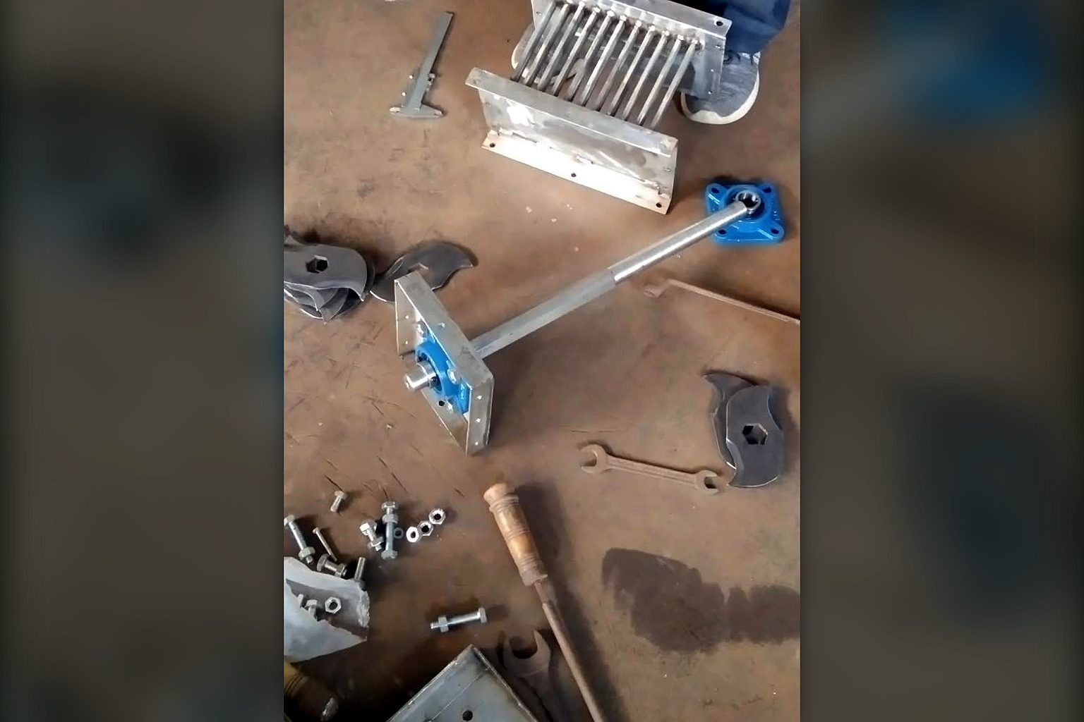 Composter agitator shaft with plummer block bearings, granulator knife set and drive parts laid out on the workshop floor before assembly