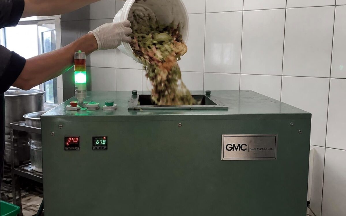 Kitchen staff tipping segregated vegetable and food waste into the top loading opening of a TGMC composter