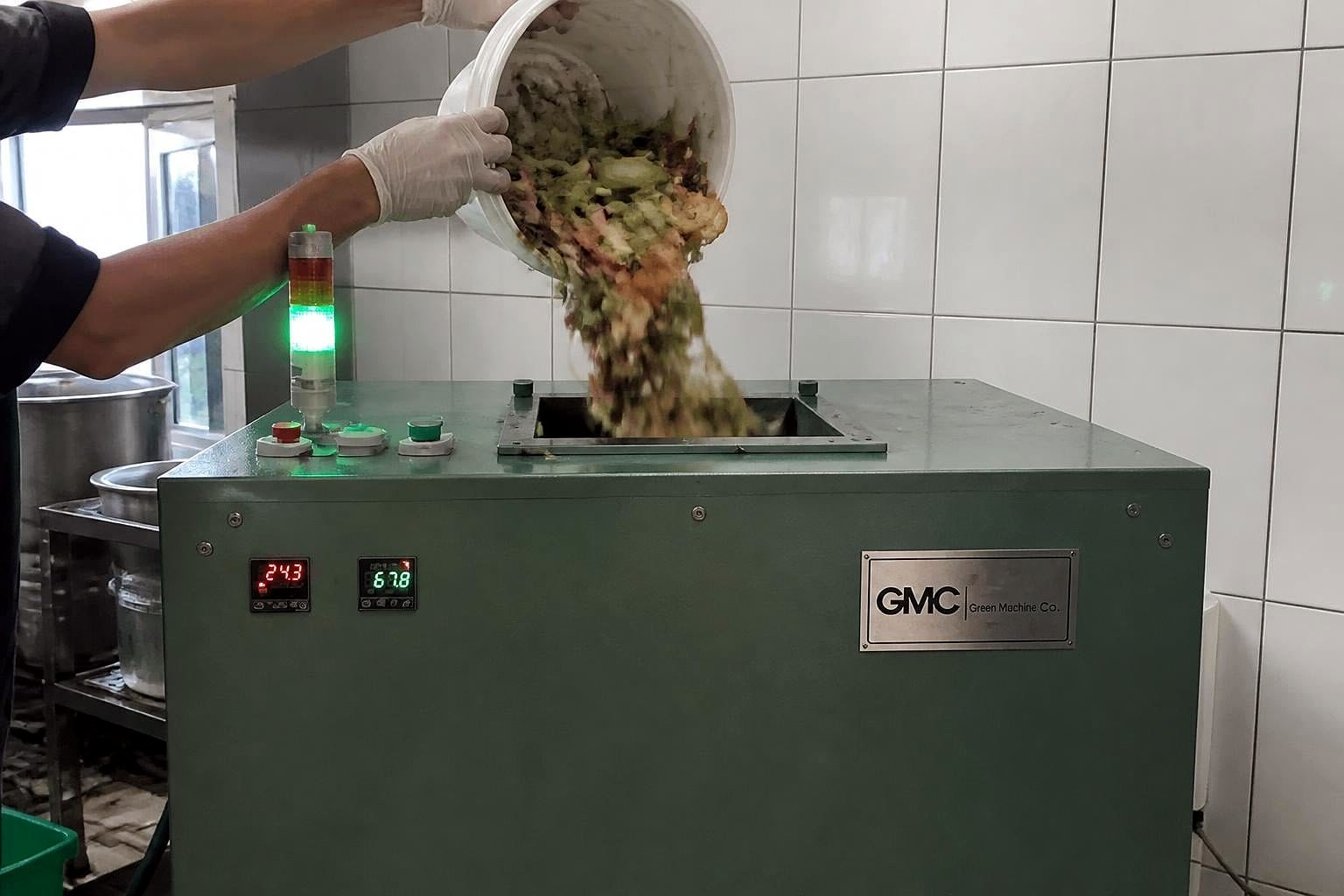 Kitchen staff tipping segregated vegetable and food waste into the top loading opening of a TGMC composter