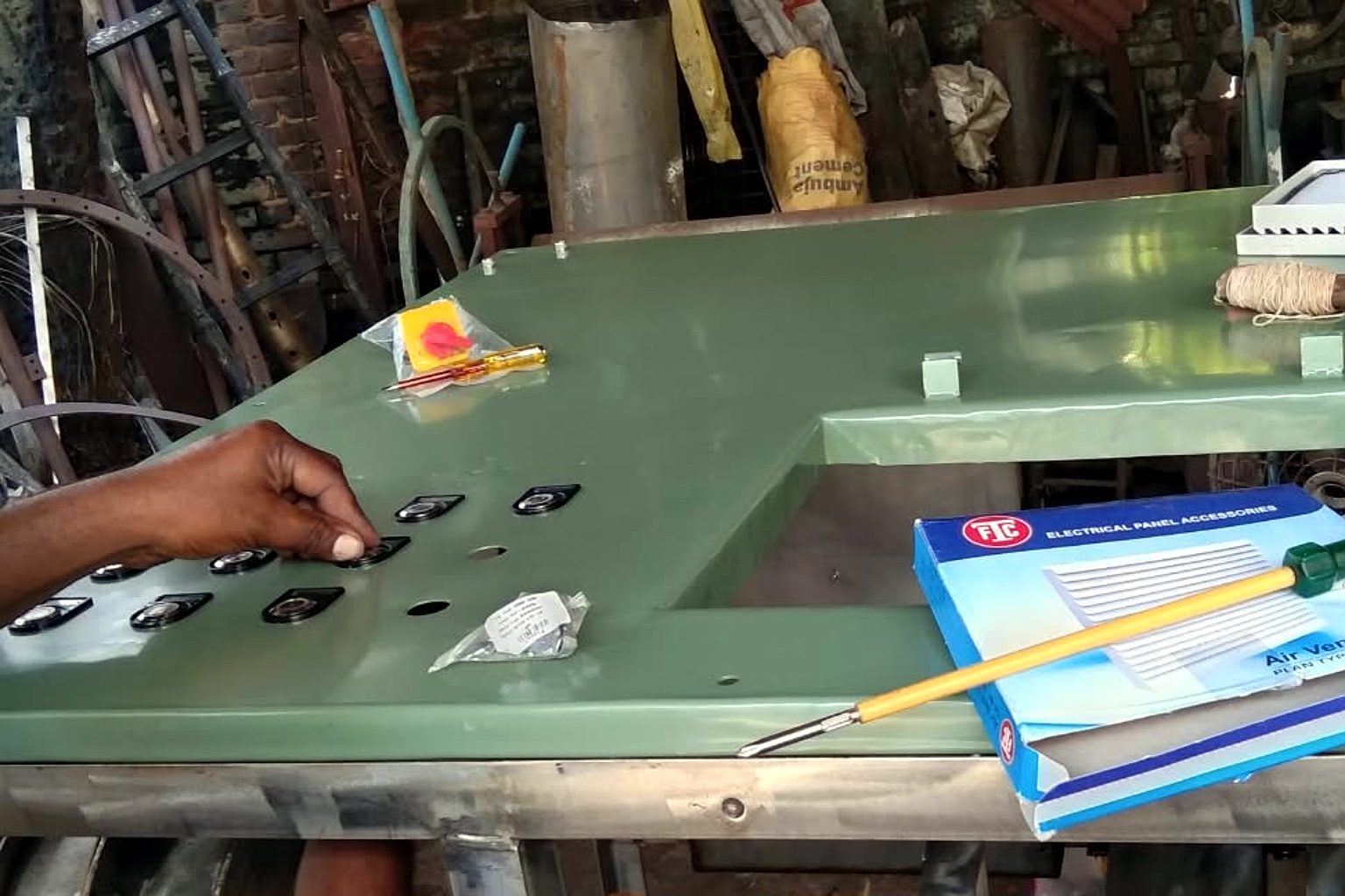 A technician’s hand fitting push buttons and indicator lamps into the green top panel of a TGMC composter at the workshop